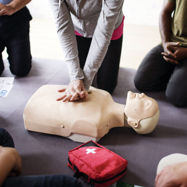 Man practicing resuscitation on a dummy within a classroom.